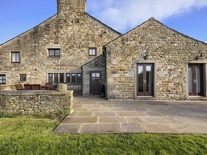 A stone building with a chimney, a door, and a patio area with chairs.