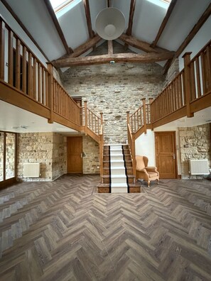 A spacious interior with a herringbone floor, wooden staircase, stone walls, and a high ceiling with exposed beams.