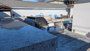 Un cortile con una griglia per barbecue, una piscina e un patio in pietra.