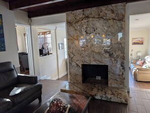 Ein Wohnzimmer mit einem Marmor-Kamin, einem schwarzen Ledersofa und einem Couchtisch mit Dekoration.