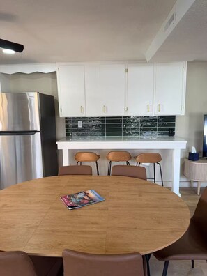 A modern kitchen with white cabinets, a stainless steel refrigerator, and a black tiled backsplash.