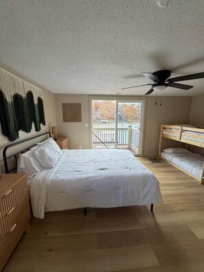 A bedroom with a large bed, a ceiling fan, a window with a view, and a bunk bed.