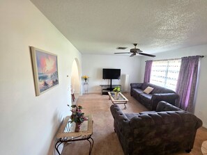 A living room with a sofa, a coffee table, a TV, and a ceiling fan.