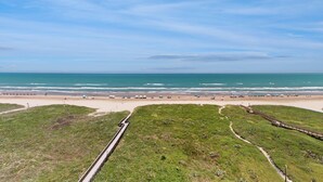 Een kustlandschap met een strand, grasvelden en een houten looppad.