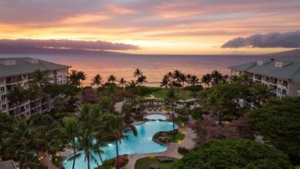Un resort con una gran piscina, palmeras y vista al océano al atardecer.