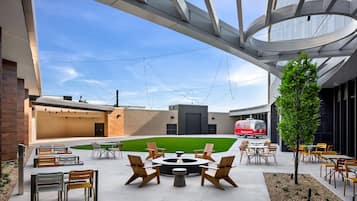 An outdoor seating area with tables and chairs, a fire pit, and a grassy lawn.