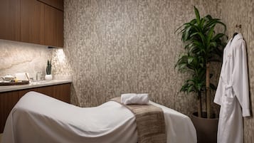 A spa room with a massage table, a towel, a robe, a plant, and a sink with toiletries.