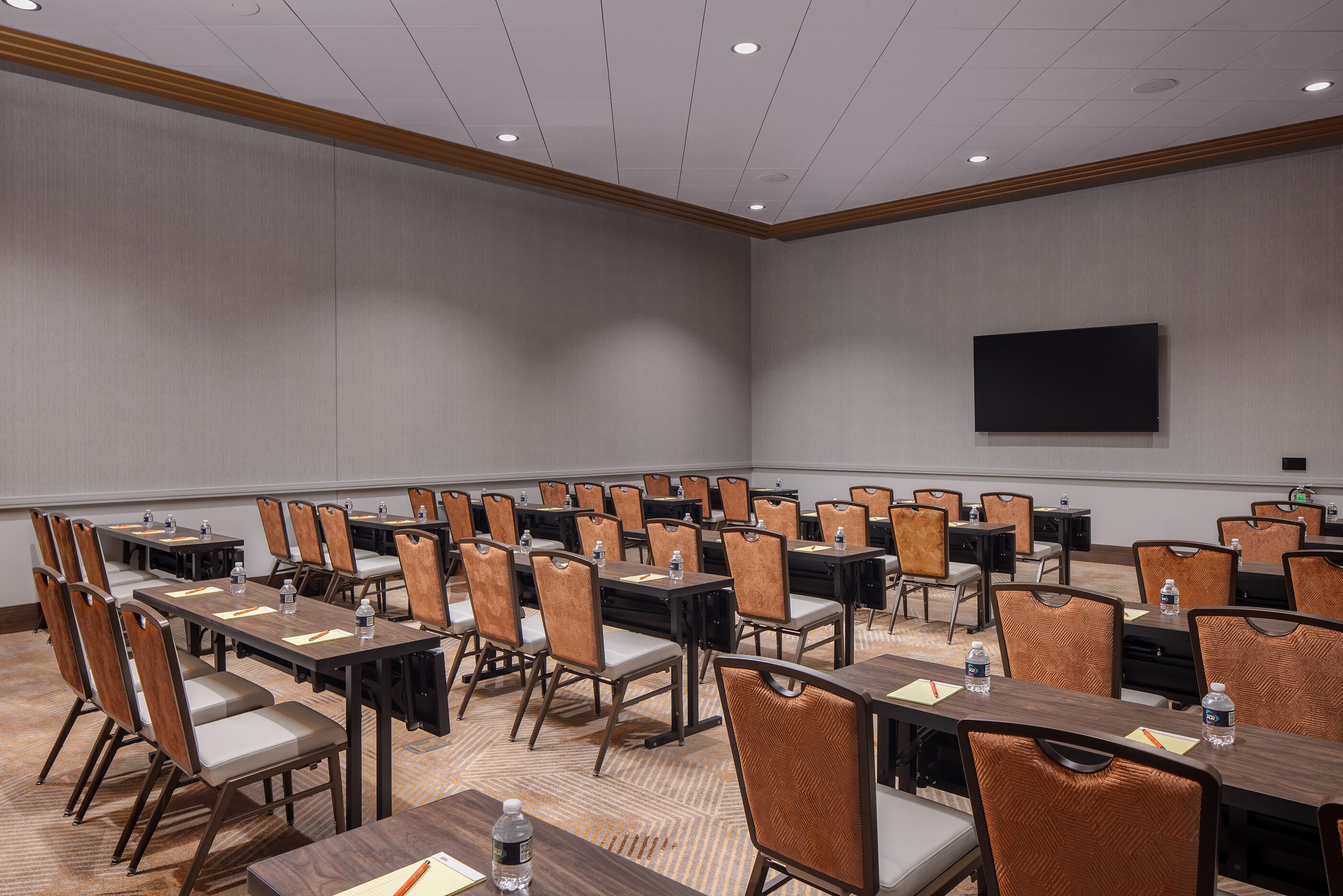Une salle de conférence avec des rangées de tables et de chaises, équipée de bouteilles d’eau et de blocs-notes.