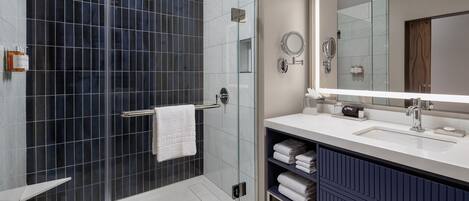Un baño moderno con ducha envuelta en vidrio, un espejo grande y un tocador con lavabo y espacio de almacenamiento.