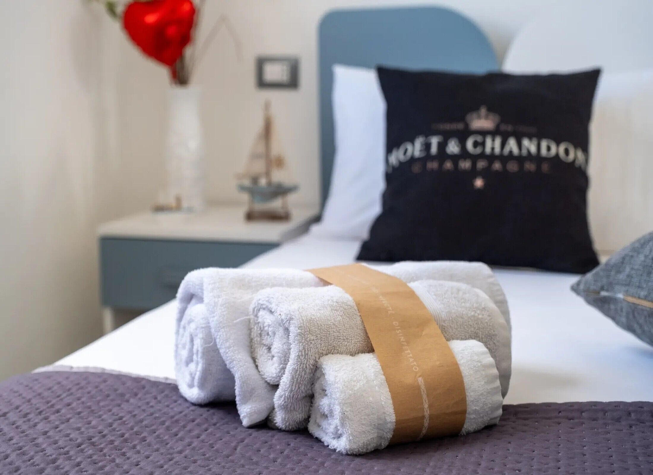 A neatly made bed with a folded towel and a pillow with 'MOËT & CHANDON' text.
