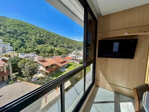 A room with a large window offering a view of a residential area and a hill. - Mirante do Oceano guesthouse, 70 meters from the beach, with a heated pool. (Bombinhas)