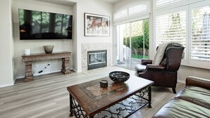 A living room with a fireplace, a television, and a large window with blinds. - Desert Escape in Indian Palms | Golf Cart Included | Near Coachella & Tennis Gardens #051797 (Indio)