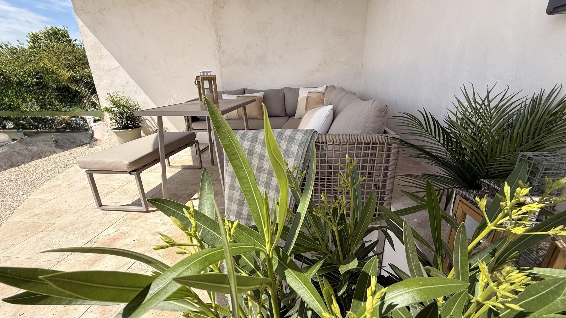 An outdoor seating area with a sofa and chairs, surrounded by potted plants.