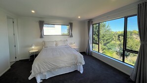 A bedroom with a large window, a bed, a nightstand, and a lamp. - Riverview Sunset Getaway - 4 bedroom 2.5 bathroom and stunning view (Hamilton)
