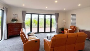 A spacious room with two orange sofas, a small round table, a wooden dresser, and a large sliding glass door leading to a balcony with greenery. - Riverview Sunset Getaway - 4 bedroom 2.5 bathroom and stunning view (Hamilton)
