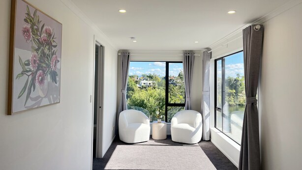 A modern room with a large window, two white armchairs, a small side table, and a painting on the wall. - Riverview Sunset Getaway - 4 bedroom 2.5 bathroom and stunning view (Hamilton)