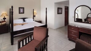 Quarto de hotel com cama de dossel, área de estar com uma cadeira, cômoda, espelho e ventilador de teto.