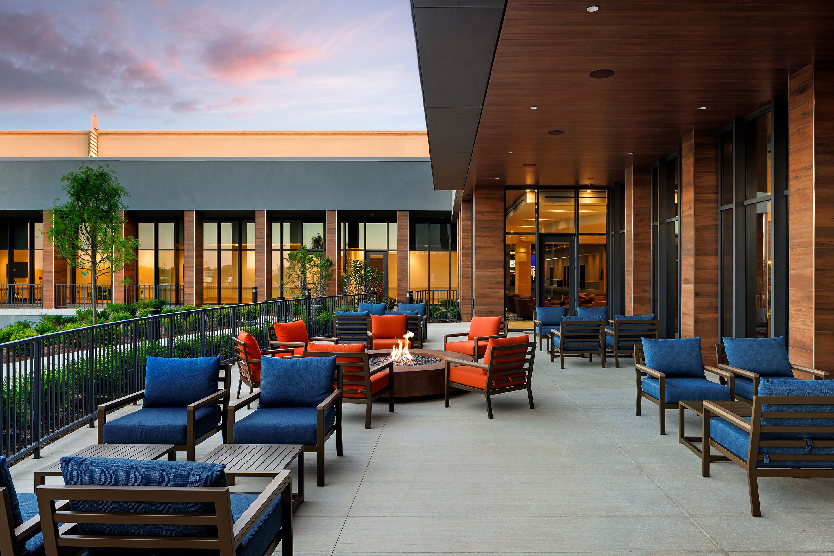 An outdoor seating area with multiple tables and chairs, a fire pit, and a view of the building's entrance.