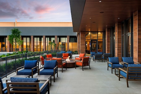 An outdoor seating area with multiple tables and chairs, a fire pit, and a view of the building's entrance.