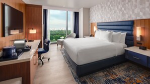 Habitación de hotel con cama, escritorio, silla y ventanas grandes.
