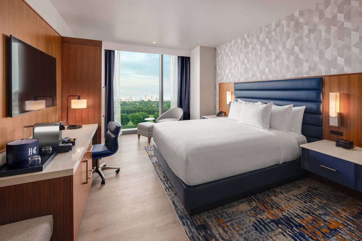Een hotelkamer met een bed, bureau, stoel en grote ramen.