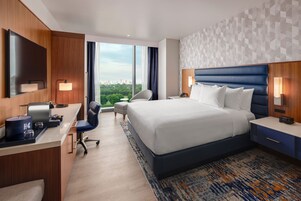 A hotel room with a bed, desk, chair, and large windows.