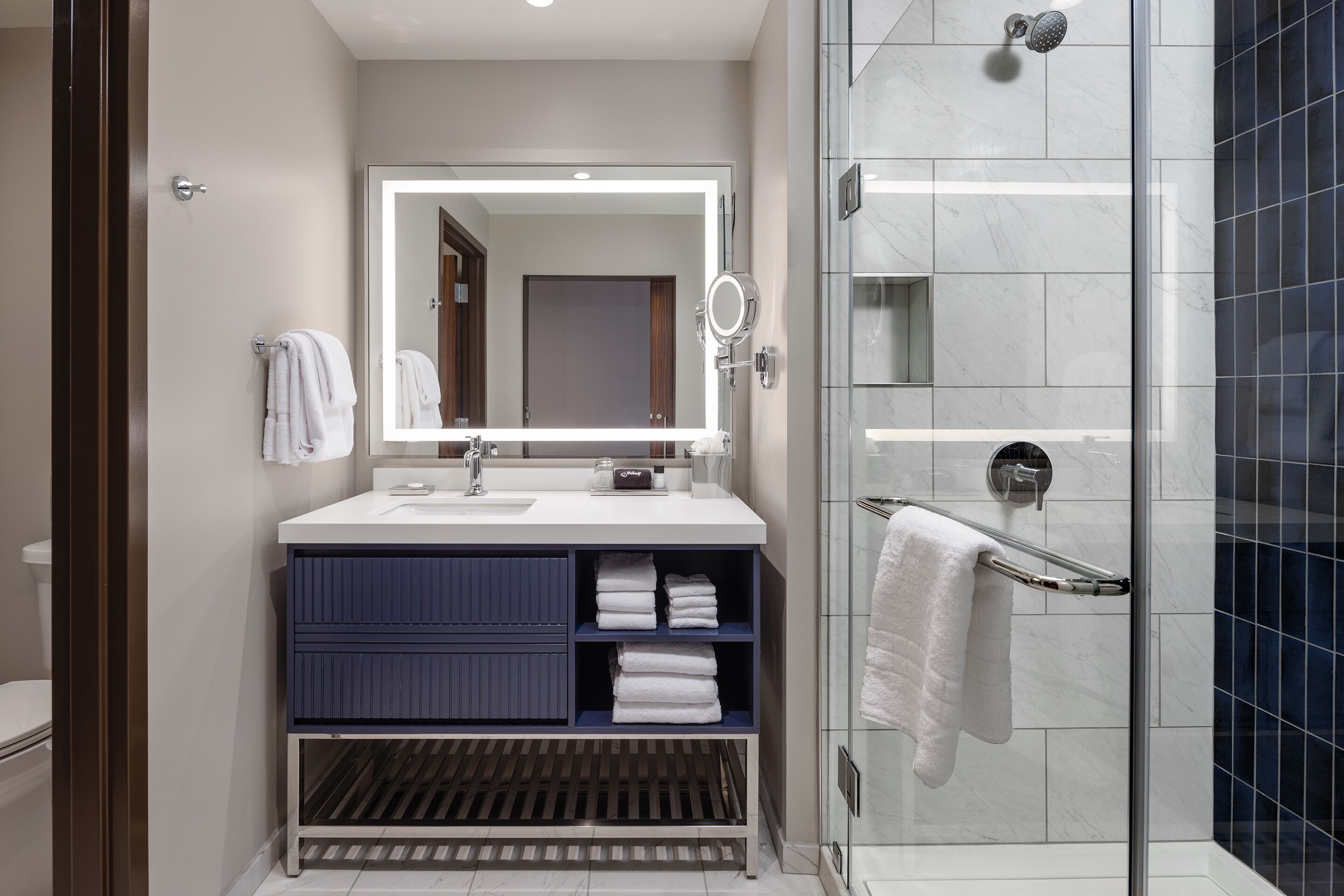 Un baño moderno con un espejo grande, una ducha y un mueble de tocador con lavamanos y toallero.
