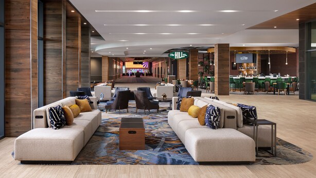 Un moderno vestíbulo de hotel con sofás, sillones, una zona de bar y un mostrador de recepción.