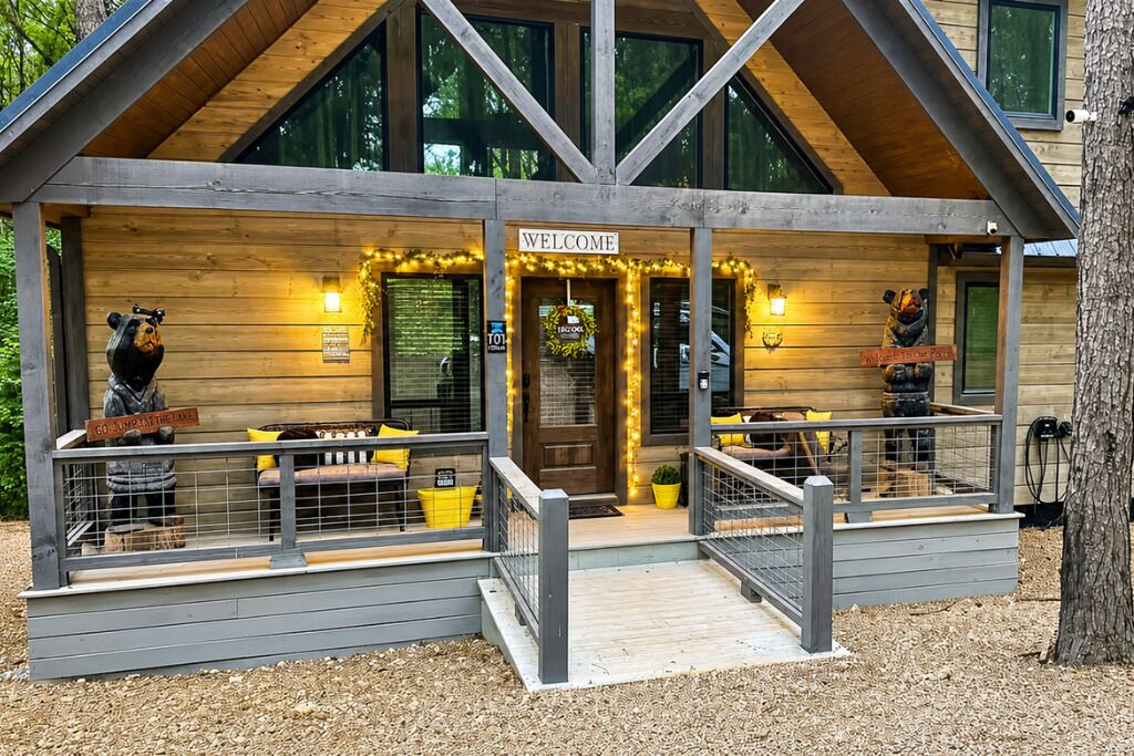 A wooden lodge with a 'WELCOME' sign, a bench, and a fenced area with a bear statue.