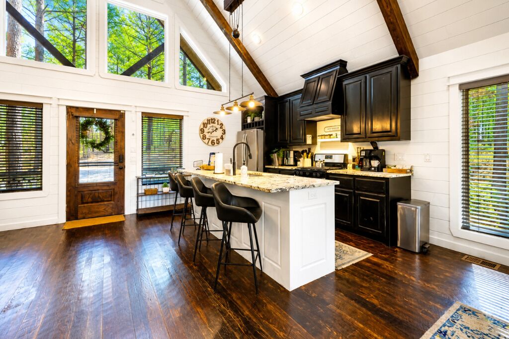 A spacious kitchen with a large island, dark wood flooring, and a view of trees through the windows.