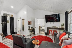A modern living room with a flat-screen TV, a sofa, a coffee table, and a red patterned rug. - Luxe Game Cabin: Pool Table + Arcade + Nintendo, Hot Tub & EV Charger (Hochatown)