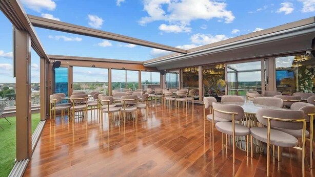 A spacious indoor area with a wooden floor, multiple seating arrangements, and large windows offering a view of the sky and distant landscape. - Stylish Ensuite Double Room Near Ilford Station (Ilford)