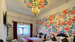 A hotel room with two beds, a chandelier, a floral wall mural, and a wicker basket with towels. - Casona Dorada Hotel (Cusco)