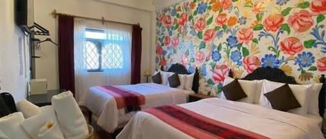 A hotel room with two beds, a chandelier, a floral wall mural, and a wicker basket with towels.