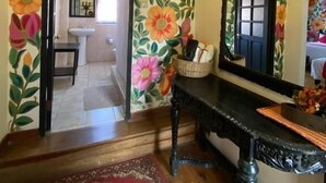 A room with a floral wallpaper, a wooden floor, a black console table, and a mirror. - Casona Dorada Hotel (Cusco)