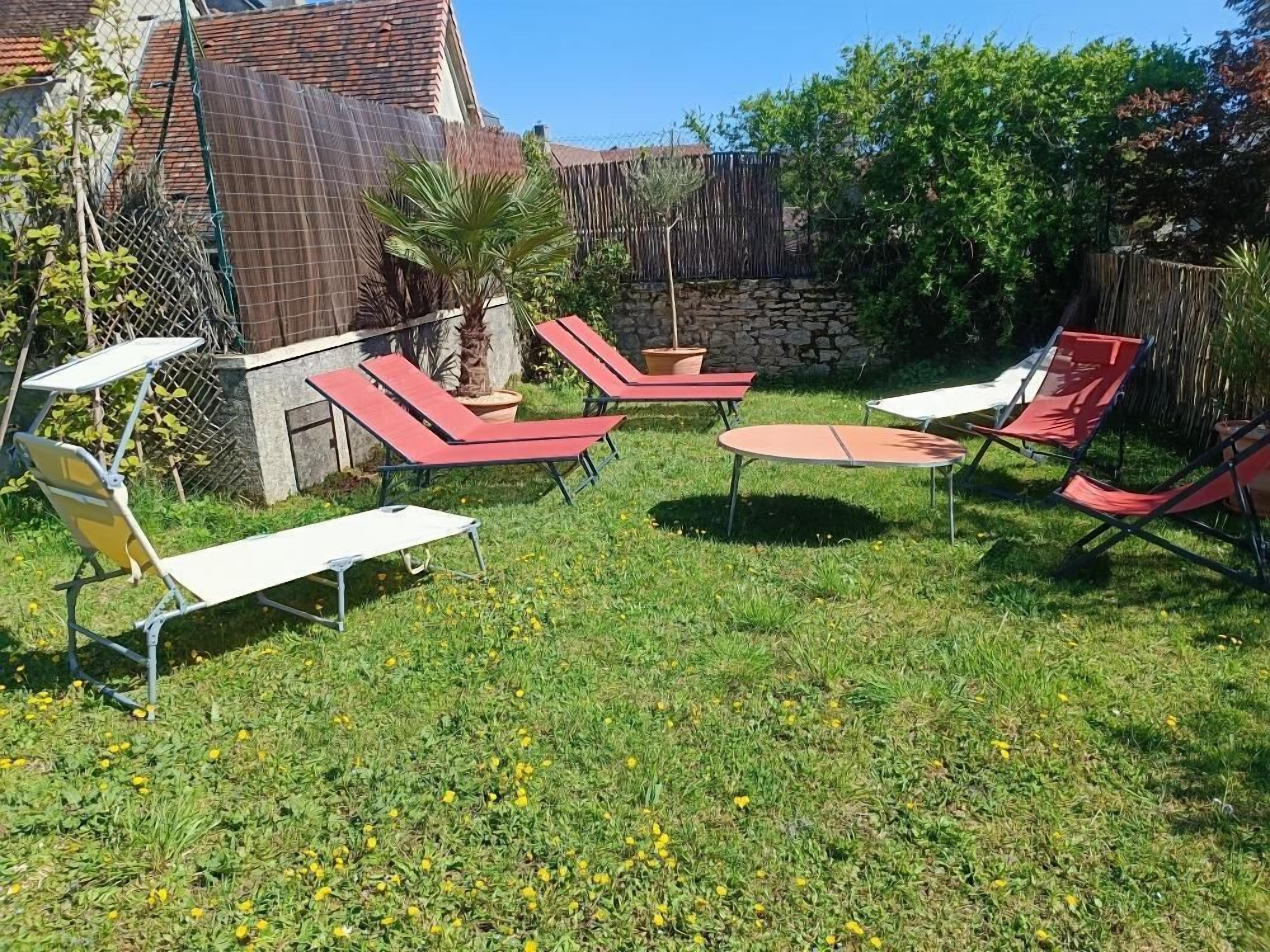 Un jardin aménagé avec du mobilier d’extérieur, notamment des chaises longues et une table, entouré d’un mur de pierres et de verdure.