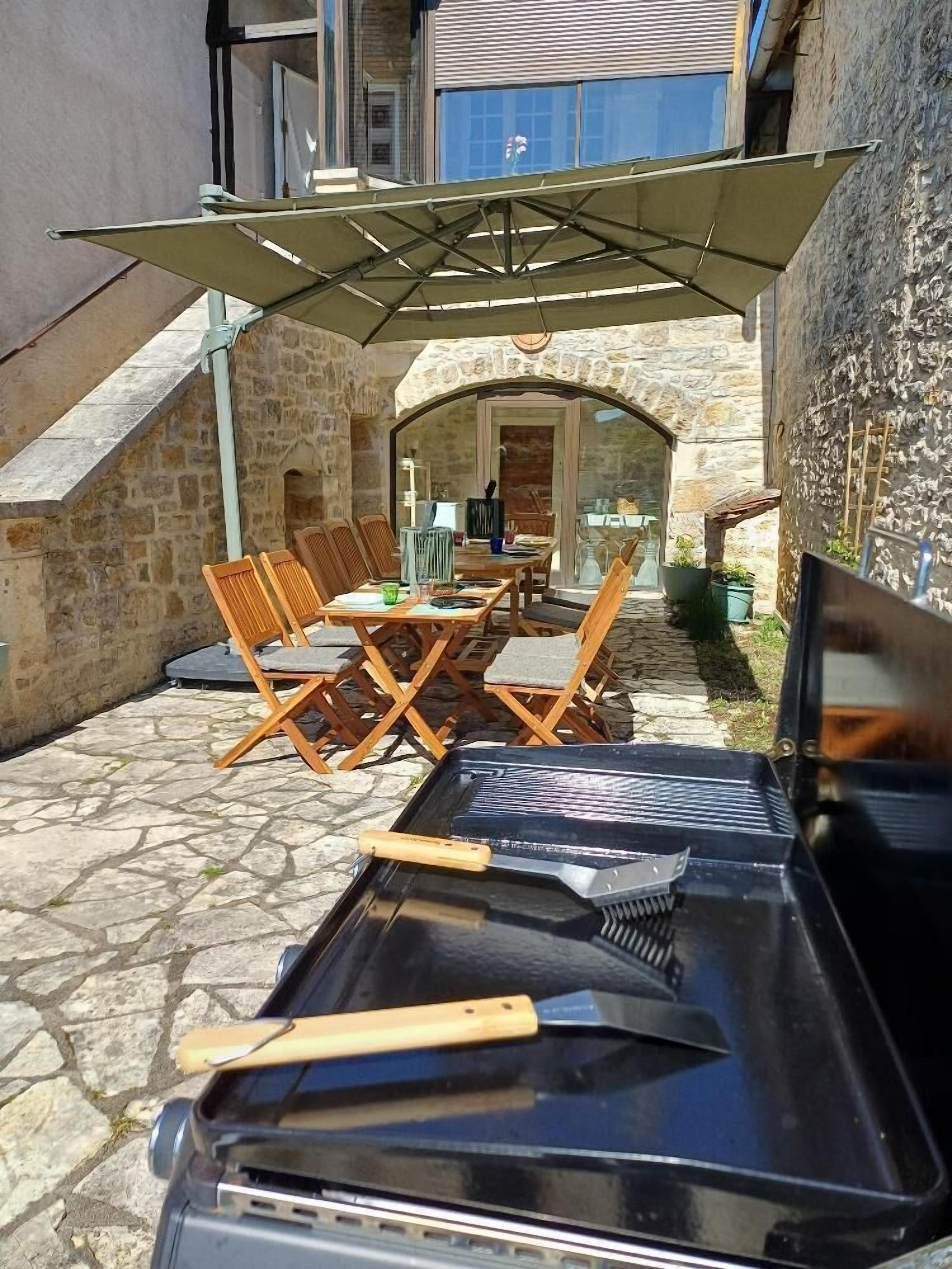 Une terrasse en pierre avec une table et des chaises, un camion noir rempli d’outils et un mur en pierre.