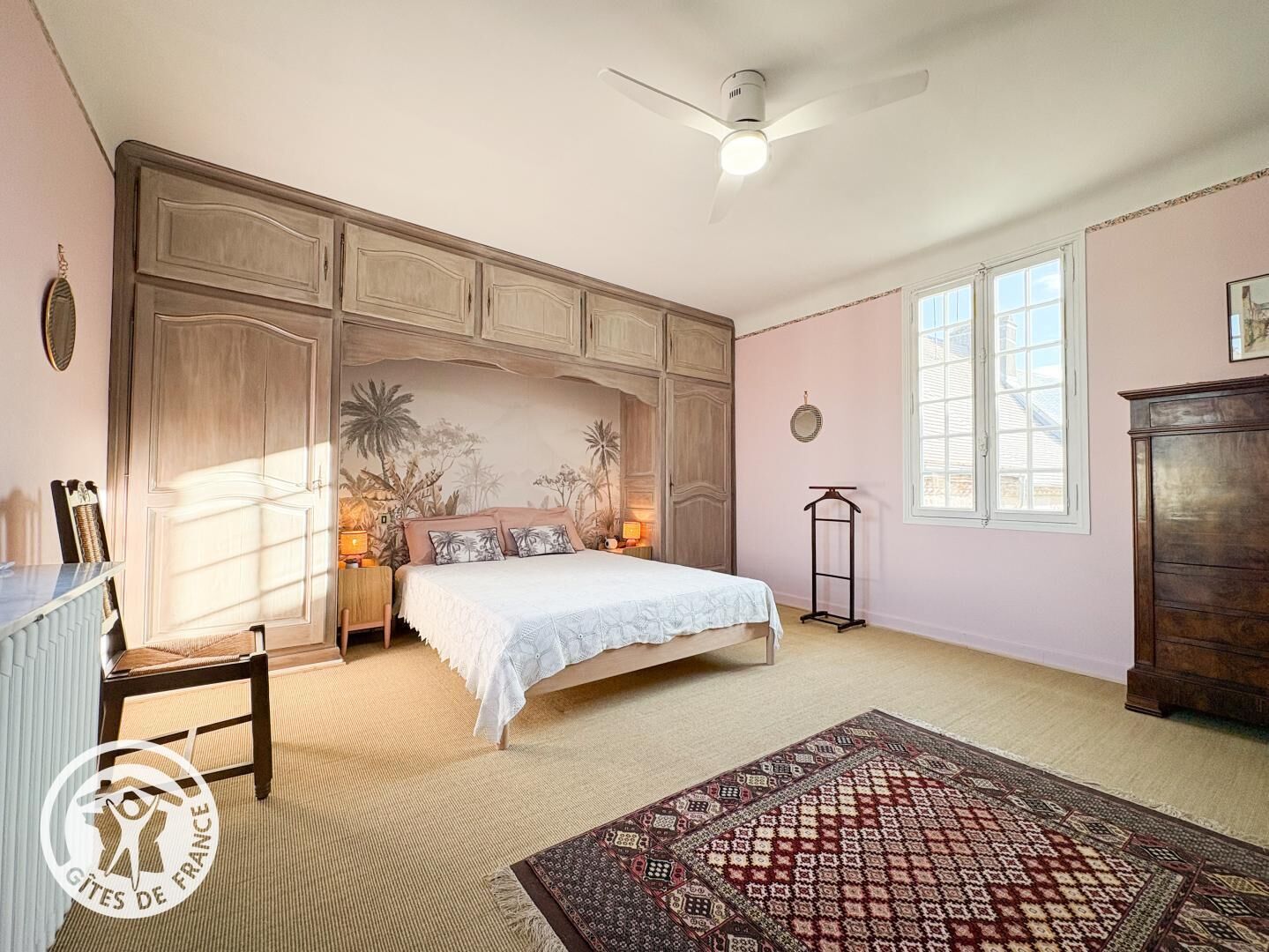 Une chambre à coucher comprenant un lit, un bureau, une chaise, une lampe sur pied, une lampe de table, un ventilateur de plafond et une fenêtre.