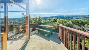 A balcony with a wooden bench and a glass door, overlooking a mountainous landscape. - Eclectic 70s Mansion (Wellington)