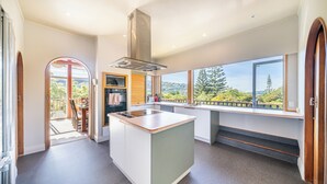 A modern kitchen with a central island, large windows, and a view of greenery. - Eclectic 70s Mansion (Wellington)