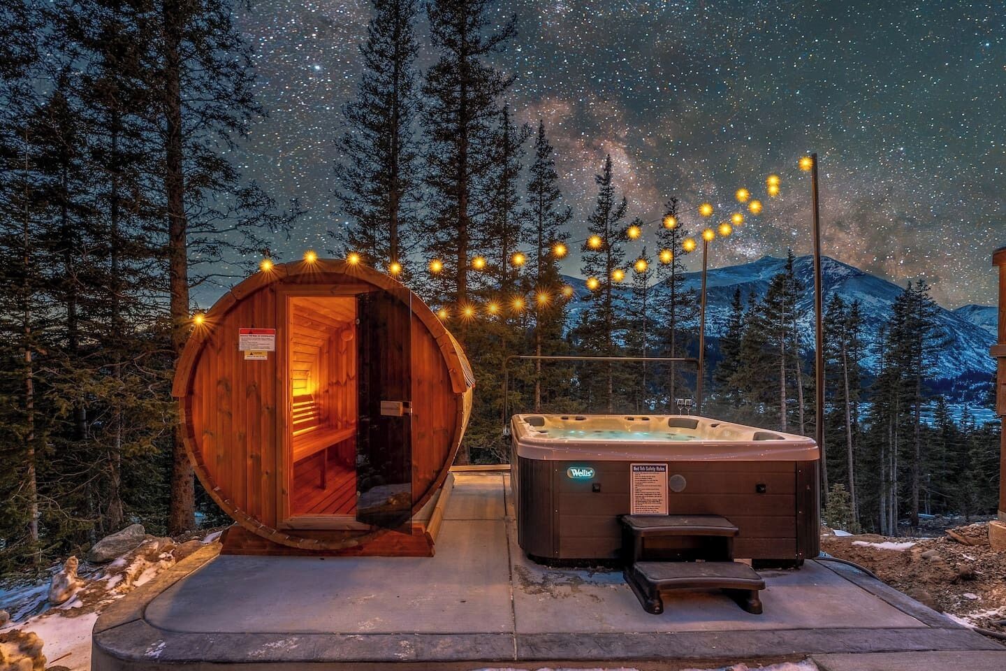 Eine Holz-Saunastruktur mit Sitzbank und Whirlpool, beschriftet mit 'Wells', in einer verschneiten Waldlandschaft bei Nacht.