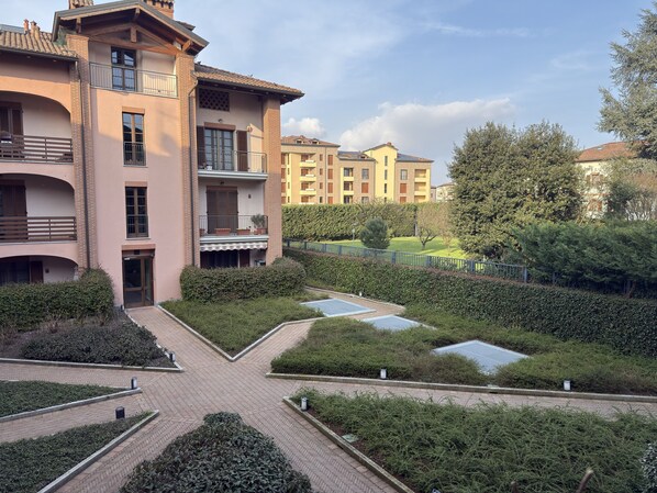 Un edificio residencial con varios balcones, un patio empedrado y abundante vegetación.