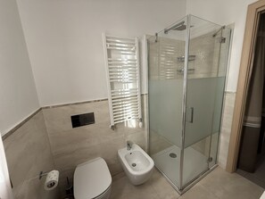 Un baño con inodoro, bidé, cabina de ducha de vidrio y un perchero para toallas.