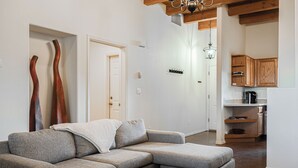 Un salon moderne avec un canapé d’angle gris, une table basse en bois et un coin cuisine doté de meubles en bois et d’un luminaire suspendu.
