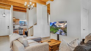 Un salon moderne doté d’un grand téléviseur à écran plat, de poutres apparentes en bois au plafond et d’un coin salon confortable.