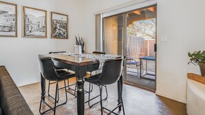 Un coin repas avec une table et des chaises, des tableaux encadrés au mur et une porte-fenêtre coulissante donnant sur un espace extérieur.