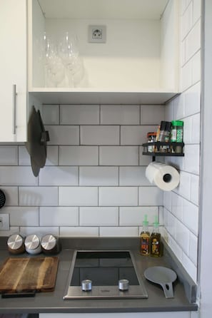 A kitchen with white tiled walls, a stainless steel stove, a wooden cutting board, a knife, a frying pan, and a spice rack. - Book Jet OASIS DUNAS Suite -apartments (Corralejo)