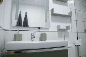 Un baño moderno con un lavabo blanco, un espejo y dos barras para toallas.