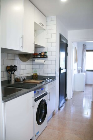 Una cocina compacta con lavadora integrada, una encimera con tabla de cortar y un lavabo.