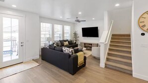 A modern living room with a black sofa, a flat-screen TV, and a staircase. - Modern Southern Utah Home: 4BR, Dog-Friendly, EV Charger (Washington)